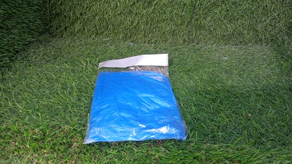 A small, clear plastic package containing a folded blue poncho rests on a vibrant green grass lawn.